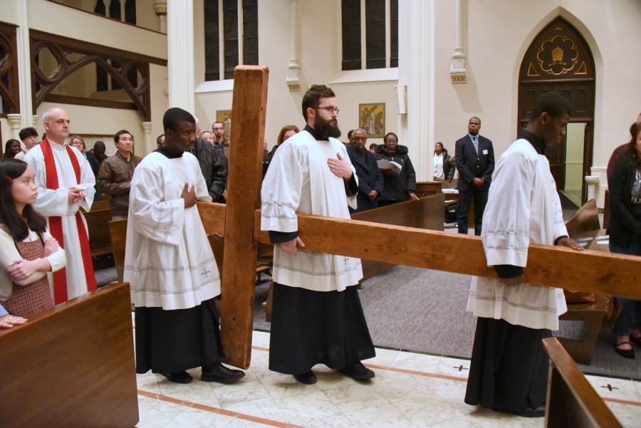 Three altar servers carry the cross