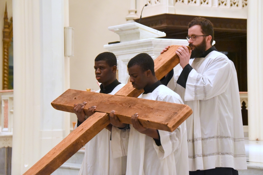 Three altar servers hold the cross.