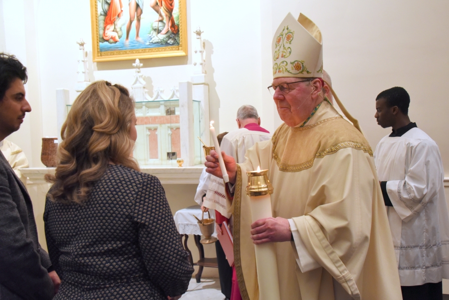 A godparent receives the baptismal candle from the bishop.
