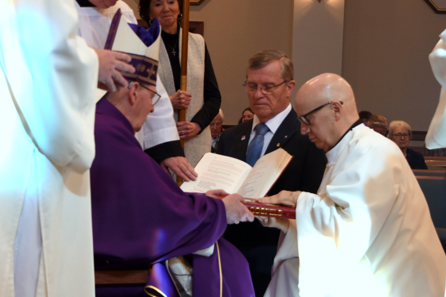 The bishop hands Deacon Mahoney the Book of the Gospels.