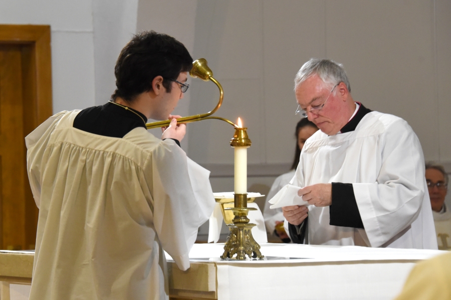The altar server lights the candles, while Msgr. Marc Caron prepares for the Liturgy of the Eucharist.