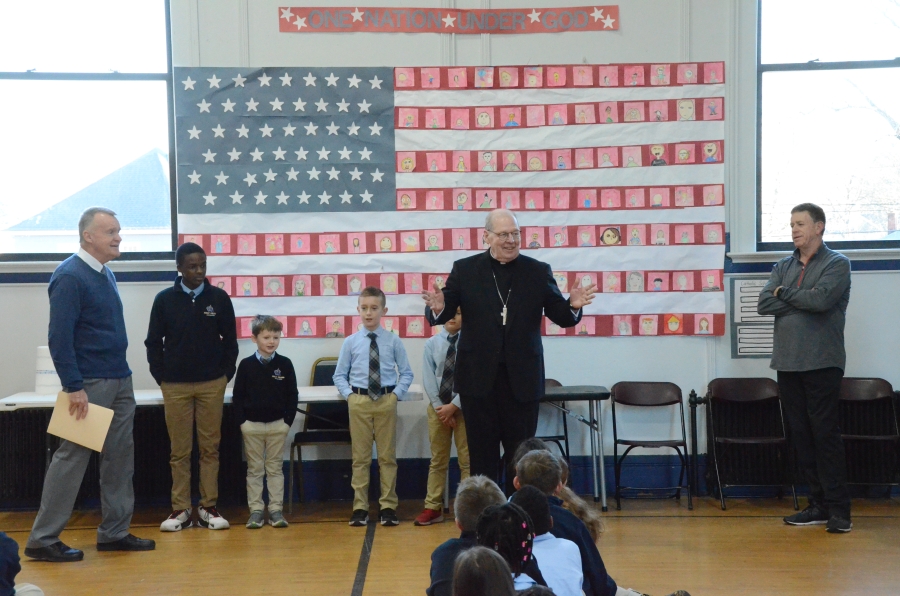 The bishop addresses students seated on the floor of a gym 