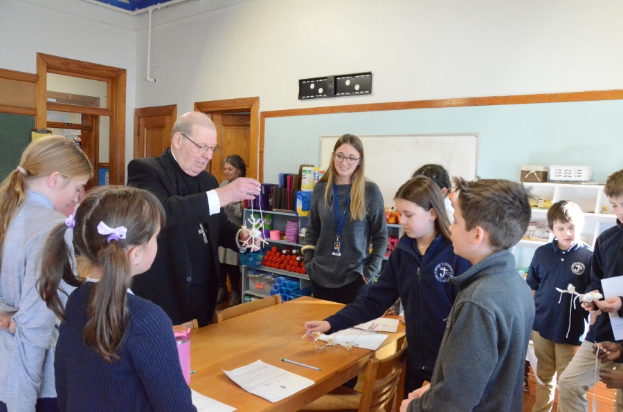 A group of students surrounds the bishop showing him projects